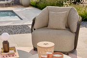 Outdoor patio with beige sofa, armchairs, and coffee table in a garden setting.