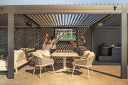 An outdoor TV on the back wall of a louvred pergola above a dining set