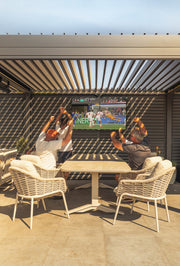 An outdoor TV fitted under a pergola with friends at the dining table